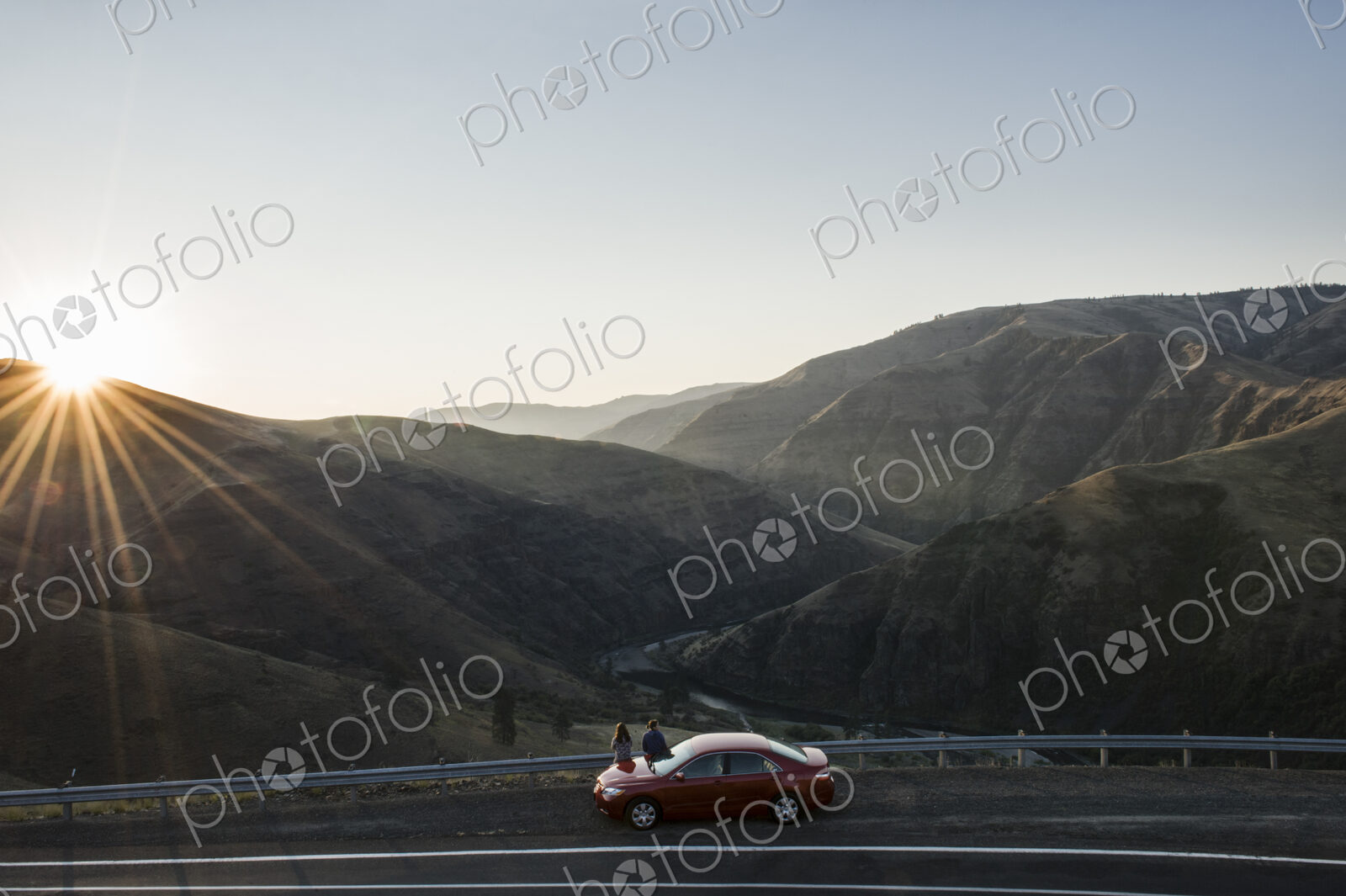 A couple watching the sunset standing next to their car at a rest stop
