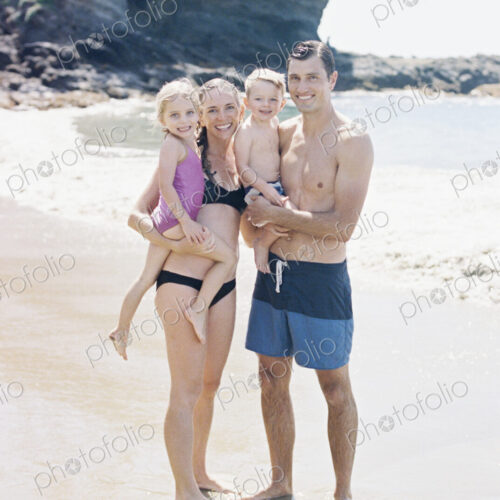 A couple with their sun and daughter, a family on the beach looking at the camera,…