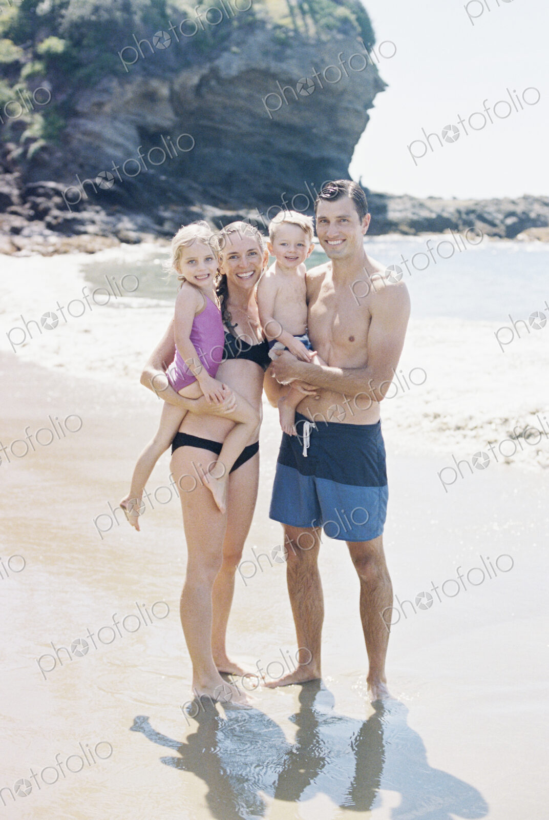A couple with their sun and daughter, a family on the beach looking at the camera,…