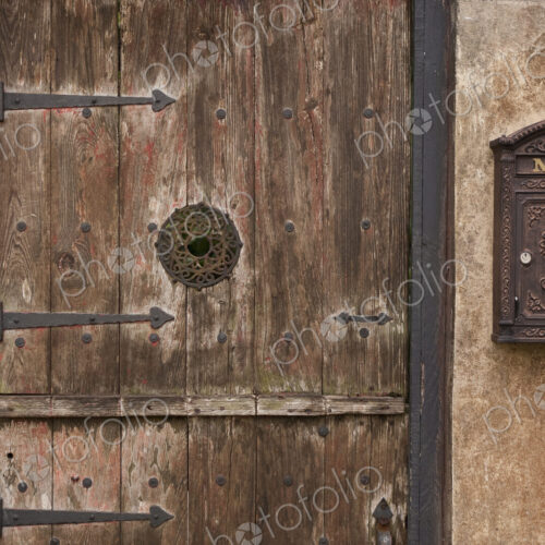 A courtyard entrance, an old wooden door with metal struts and a decorated framed spy…