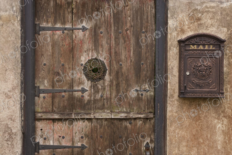 A courtyard entrance, an old wooden door with metal struts and a decorated framed spy…