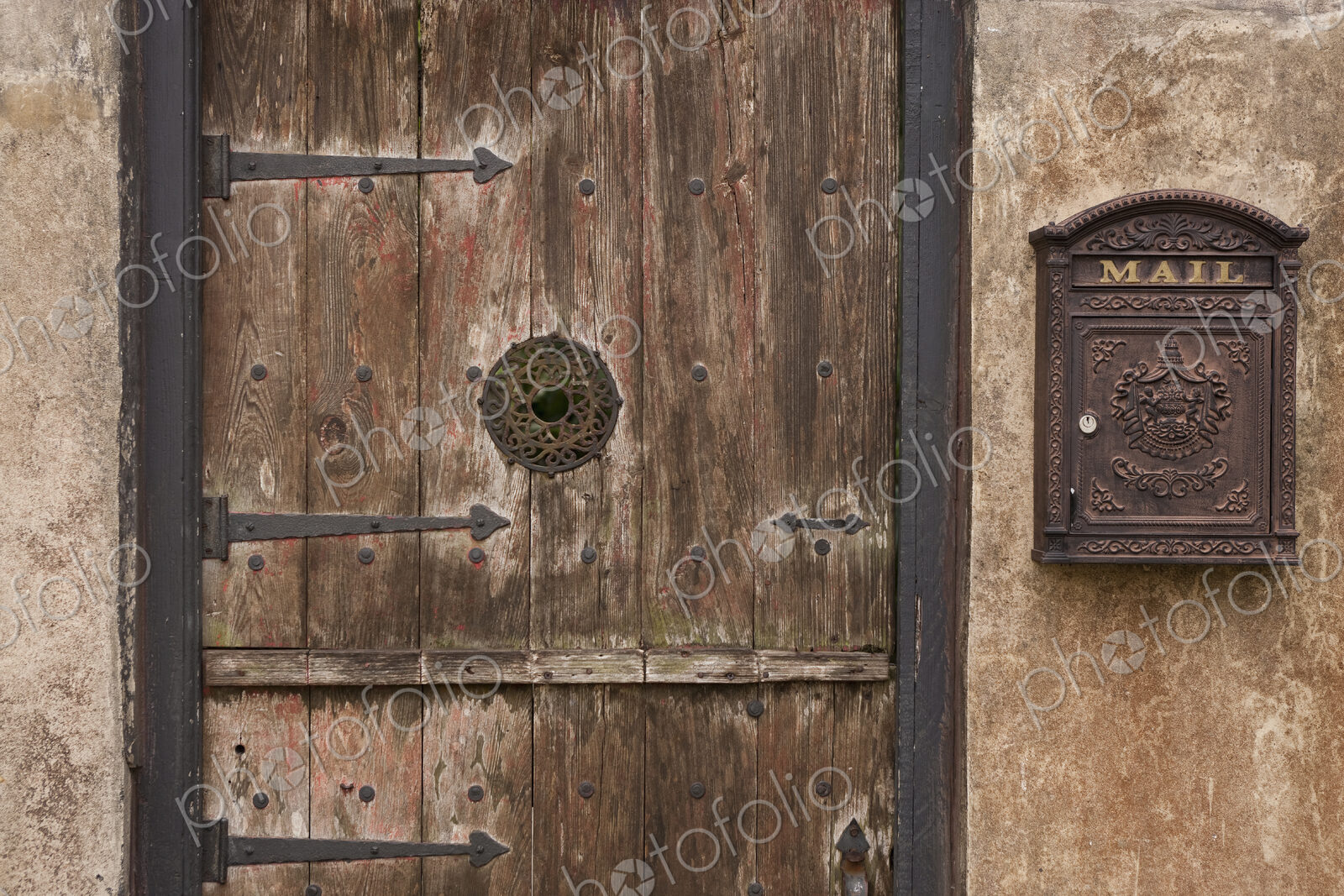 A courtyard entrance, an old wooden door with metal struts and a decorated framed spy…