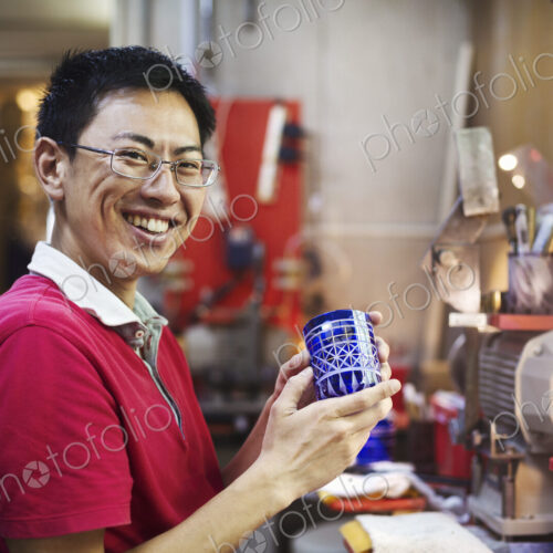 A craftsman at work in a glass maker's workshop working on a vivid blue cut glass object.