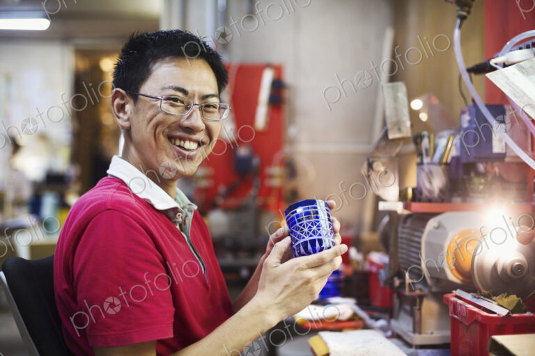 A craftsman at work in a glass maker's workshop working on a vivid blue cut glass object.