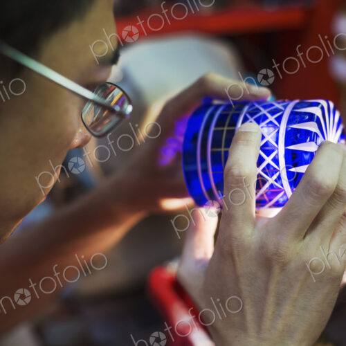 A craftsman glass maker holding a vivid blue cut glass cup, inspecting it closely.