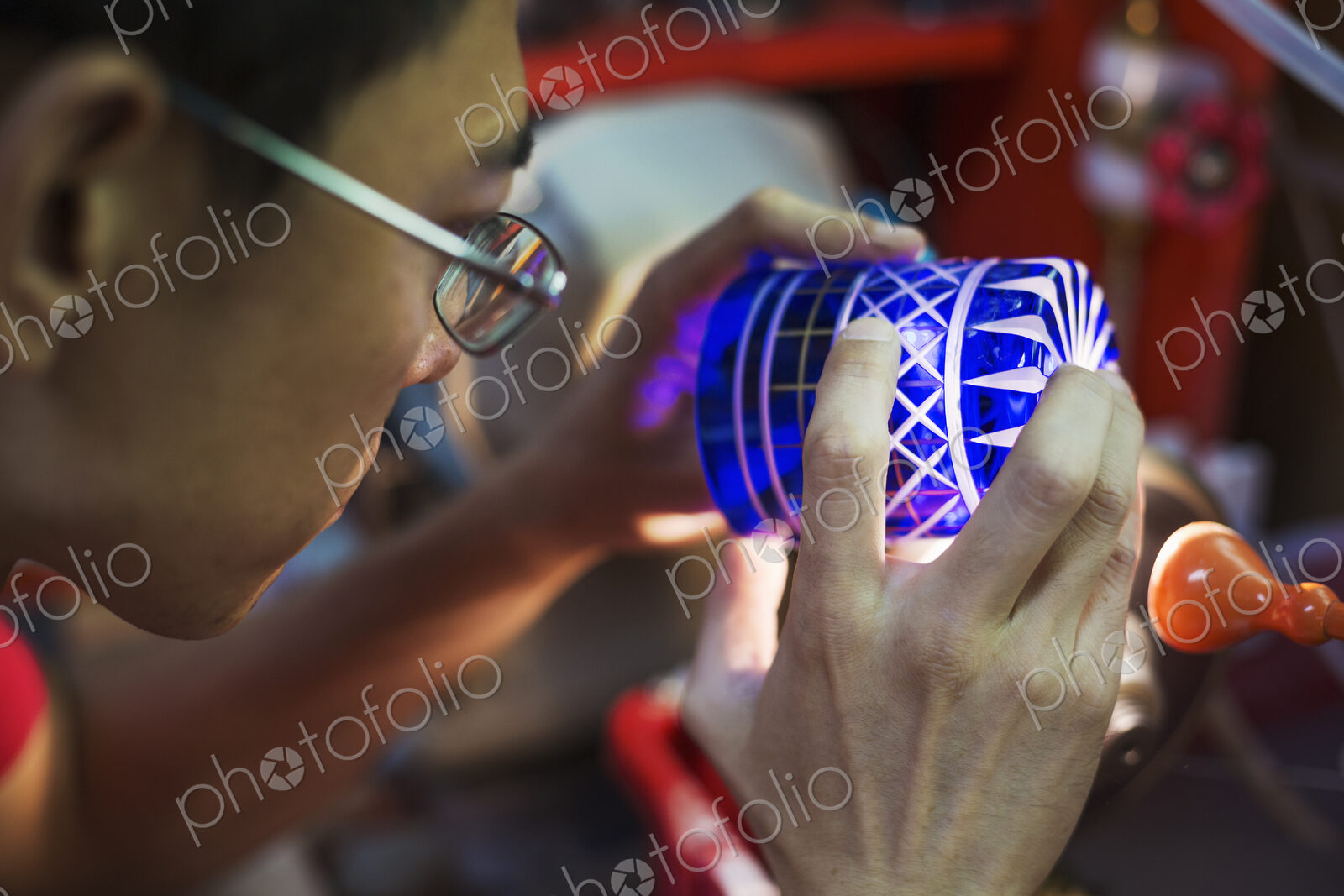 A craftsman glass maker holding a vivid blue cut glass cup, inspecting it closely.