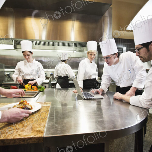 A crew of chef's working in a commercial kitchen, while several chefs wok on a laptop… A crew of chef's working in a commercial kitchen, while several chefs wok on a laptop…