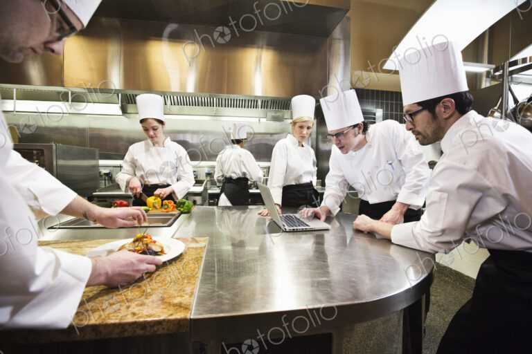 A crew of chef's working in a commercial kitchen, while several chefs wok on a laptop…