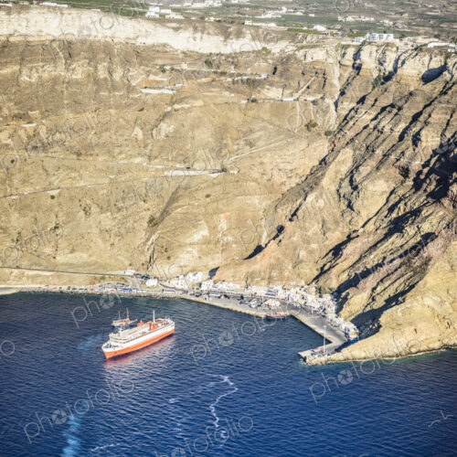 A cruise ship approaching the harbour of Oia on the coastline at the base of a steep…