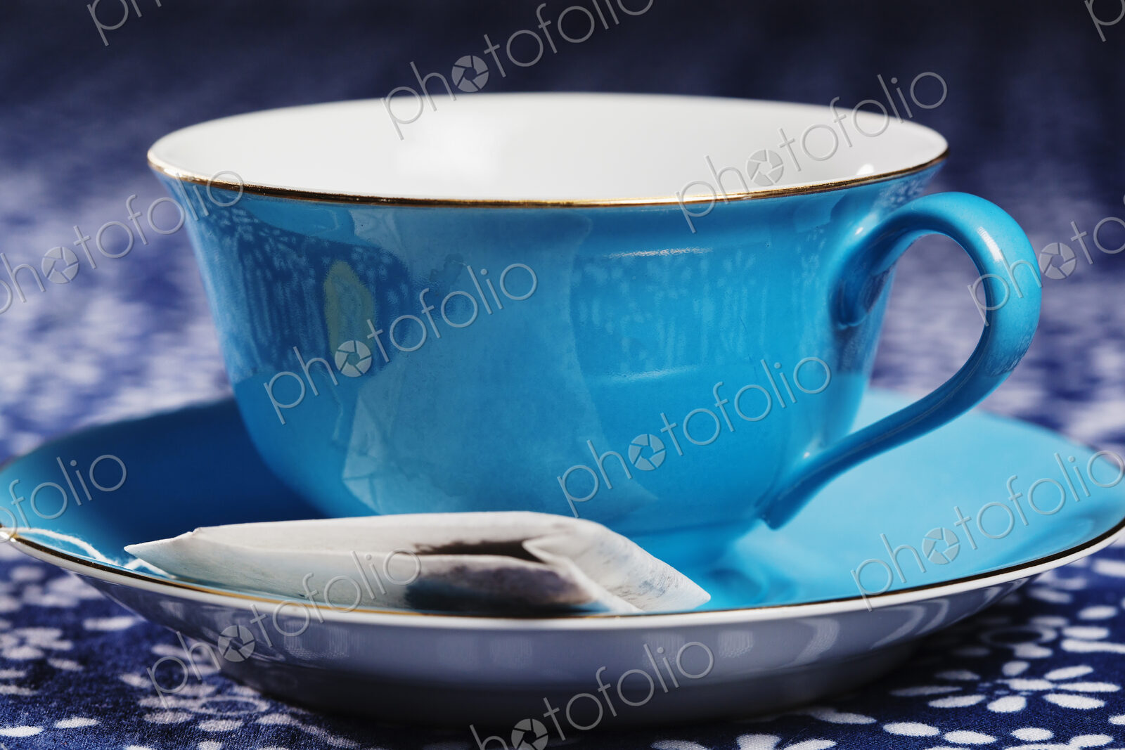 A cup and saucer, blue colour, a tea bag in the saucer.