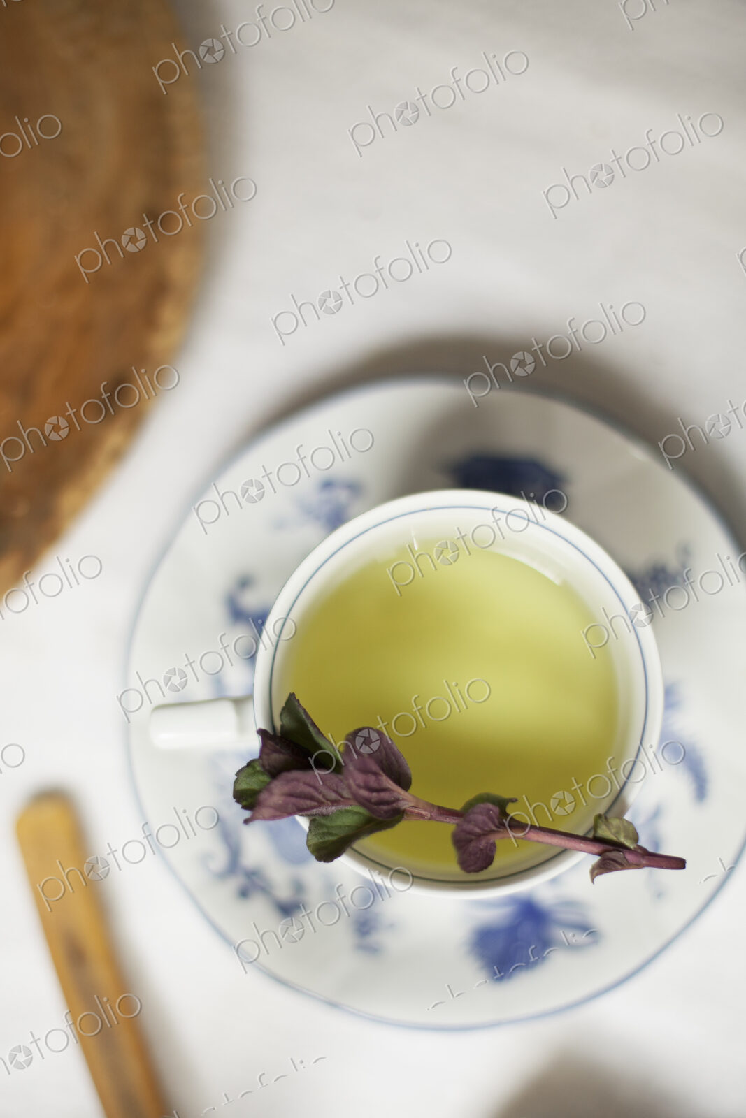 A cup of tea, clear coloured tea in a china cup, with a sprig of aromatic mint.