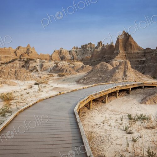 A curving boardwalk leads into eroded buttes and pinnacles under a clear blue sky in… A curving boardwalk leads into eroded buttes and pinnacles under a clear blue sky in…