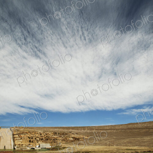 A dam wall and sluice overflow into a lake, with a blue sky and streaked cloud pattern. A dam wall and sluice overflow into a lake, with a blue sky and streaked cloud pattern.