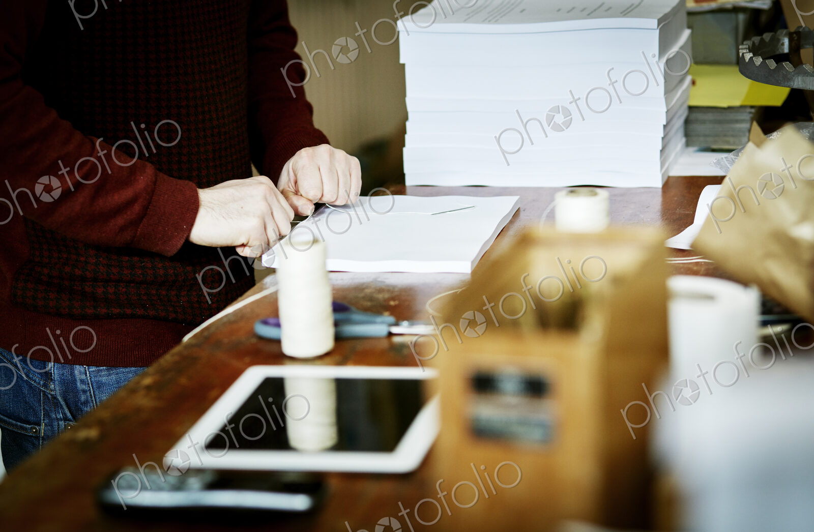A digital tablet on a workbench, and a man handstitching a pile of paper pages.