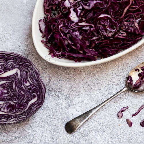 A dish of cooked red cabbage and half a raw cabbage.