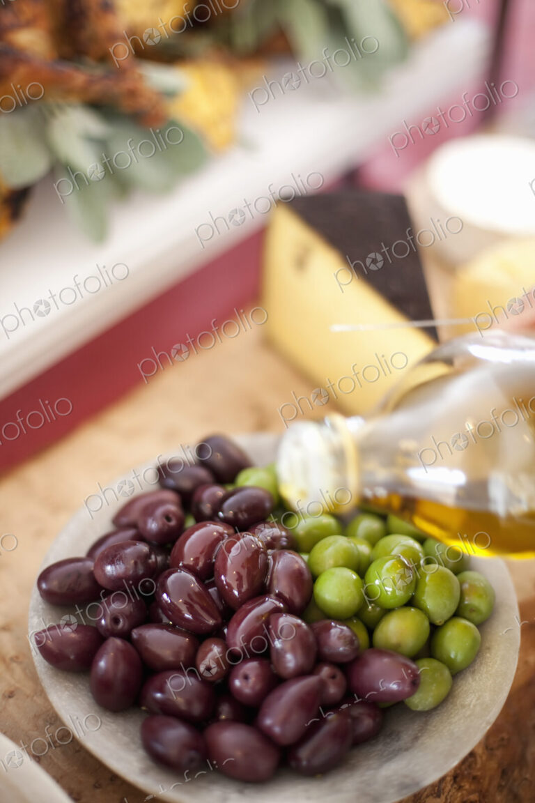 A dish of fresh organic vegetables. Green and black olives on a plate with a drizzling…