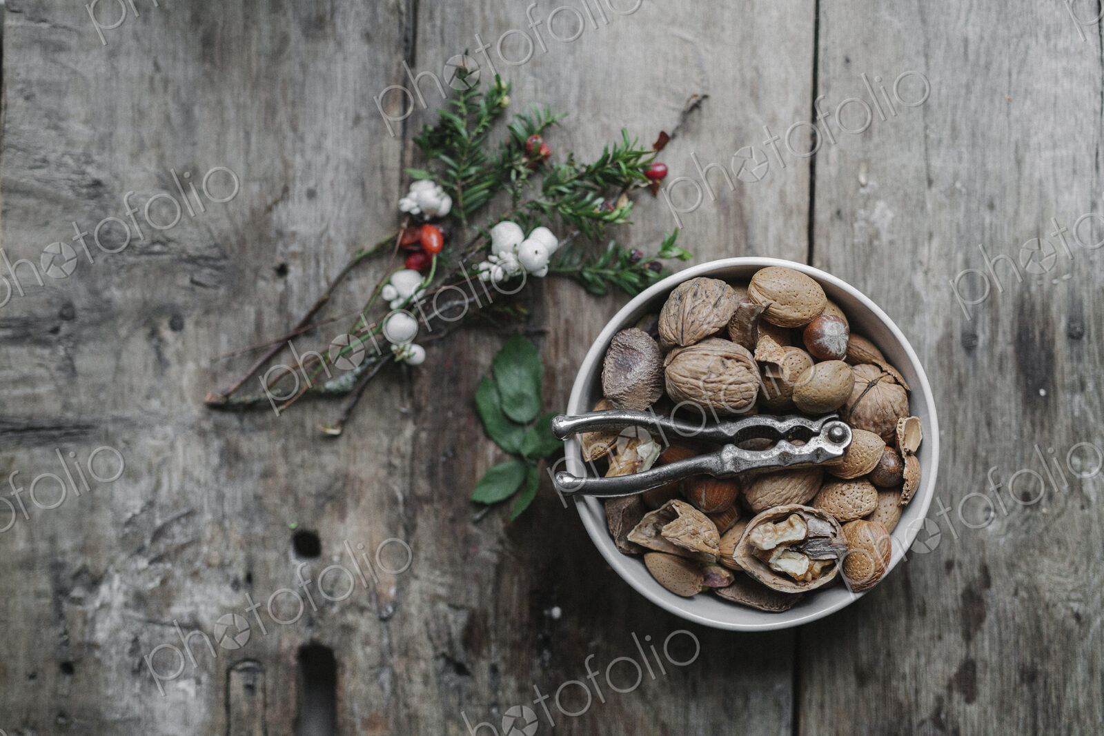 A dish of nuts and a nut cracker on a table with a sprig of yew wit red berries.