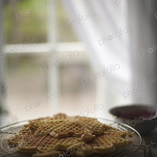 A dish of waffles on a tabletop. Net curtains draped back from a window. A dish of waffles on a tabletop. Net curtains draped back from a window.