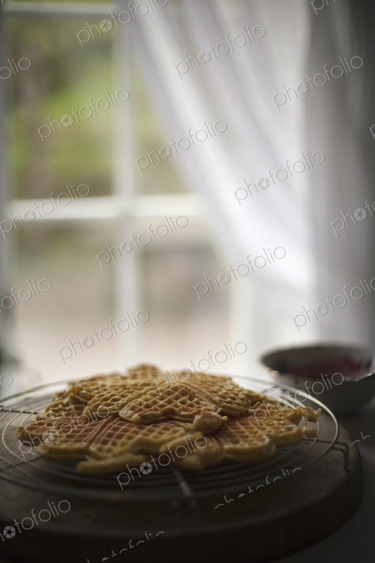 A dish of waffles on a tabletop. Net curtains draped back from a window.
