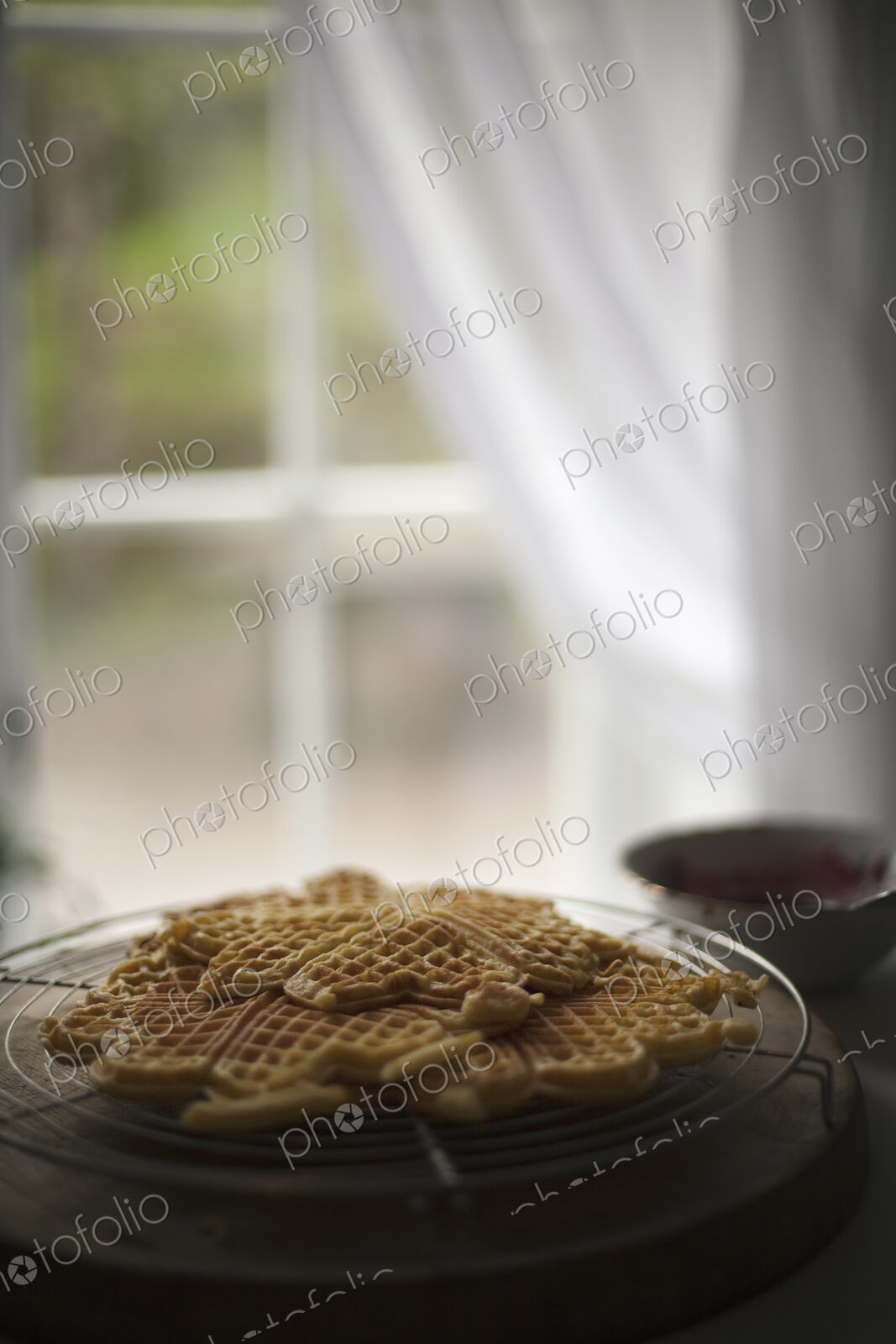 A dish of waffles on a tabletop. Net curtains draped back from a window.