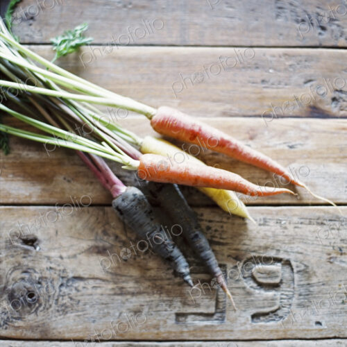 A domestic kitchen table with a worn scrubbed surface. A bunch of fresh carrots. A domestic kitchen table with a worn scrubbed surface. A bunch of fresh carrots.