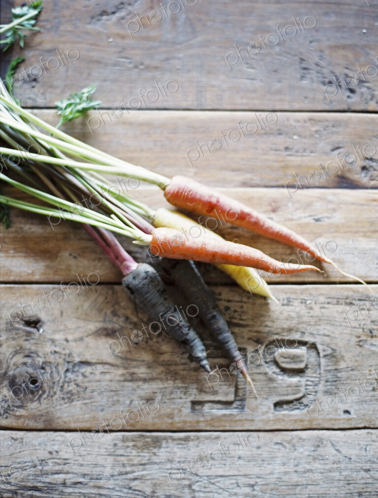 A domestic kitchen table with a worn scrubbed surface. A bunch of fresh carrots.
