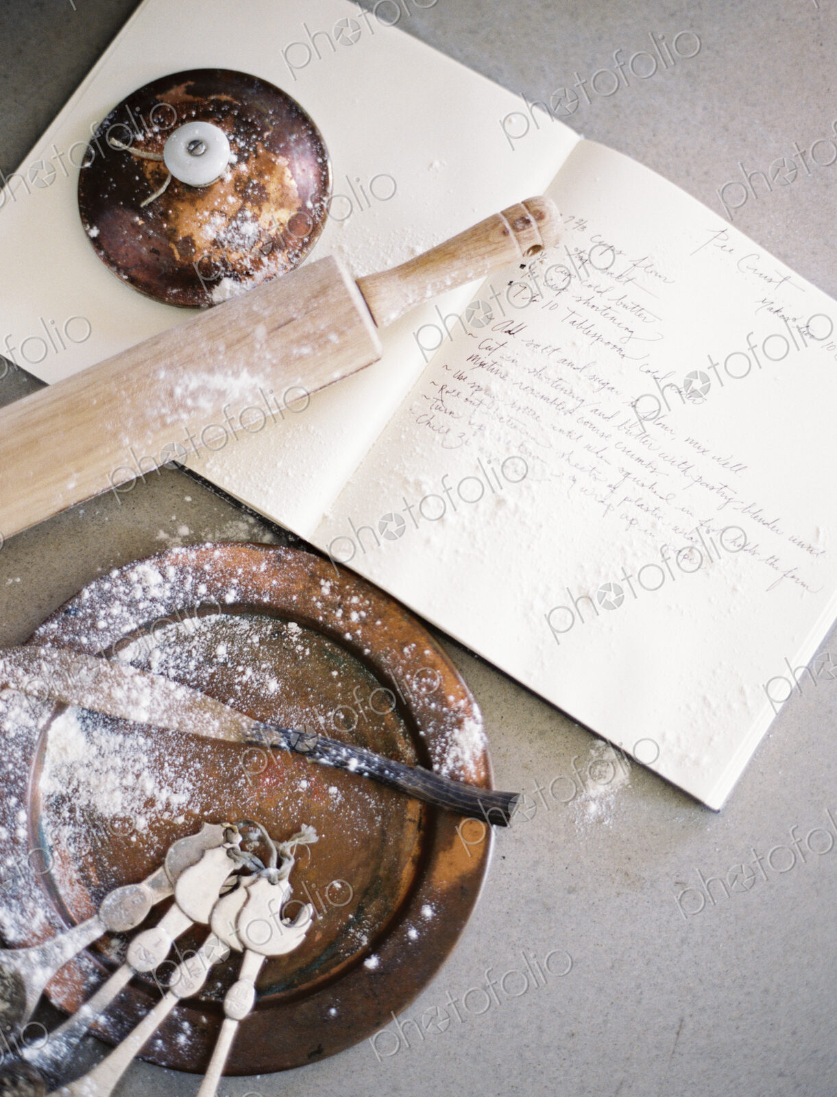 A domestic kitchen table. A large group of kitchen utensils, spoons, a pan and a…