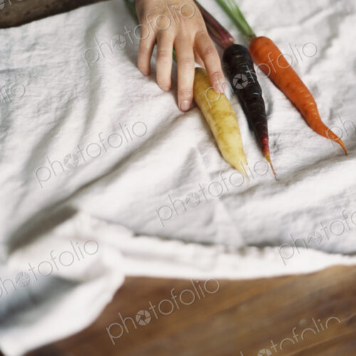 A domestic kitchen table. A person arranging fresh carrots on a white cloth. A domestic kitchen table. A person arranging fresh carrots on a white cloth.