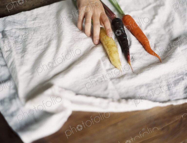 A domestic kitchen table. A person arranging fresh carrots on a white cloth.