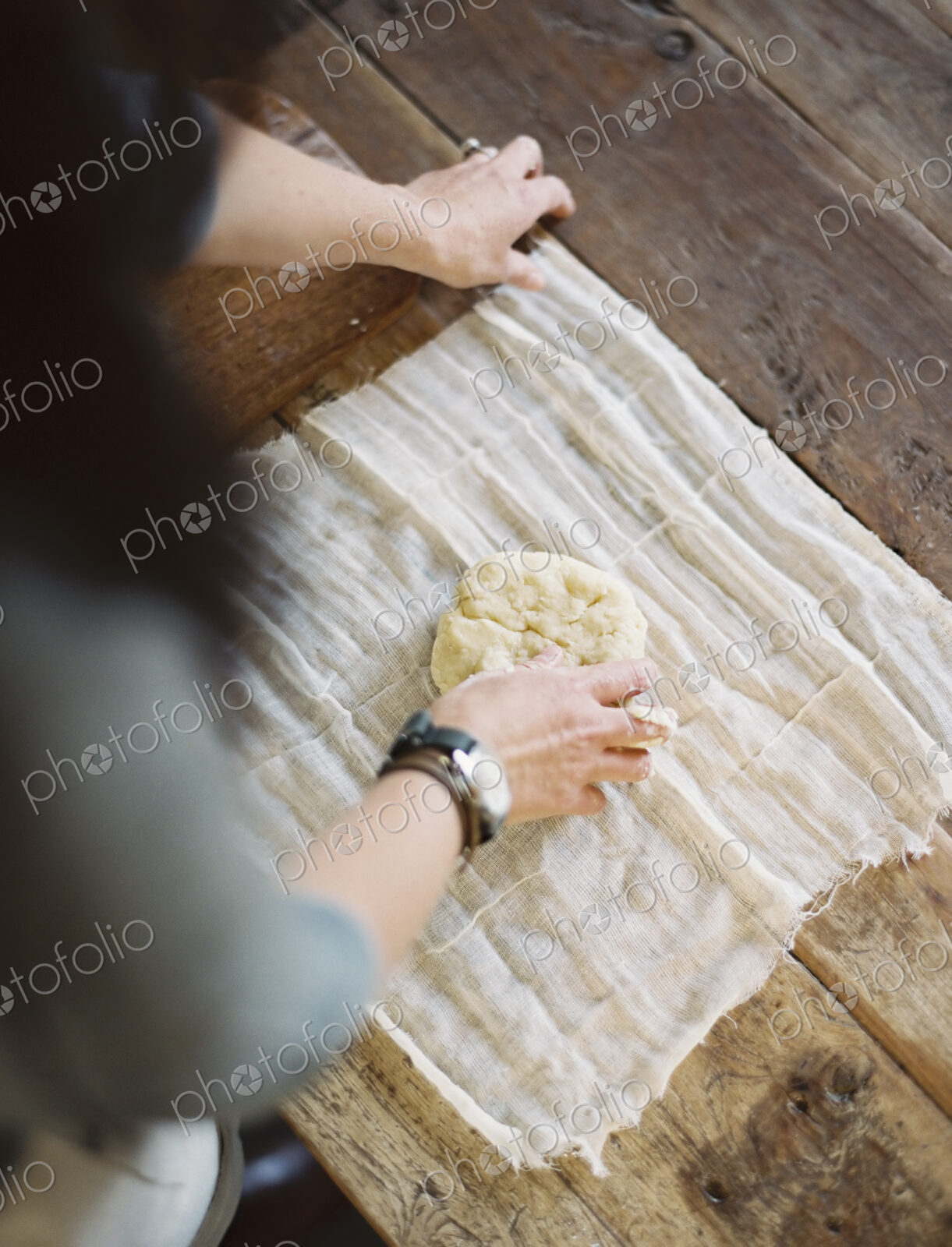 A domestic kitchen table. A view from above of a woman wrapping fresh pastry in a…