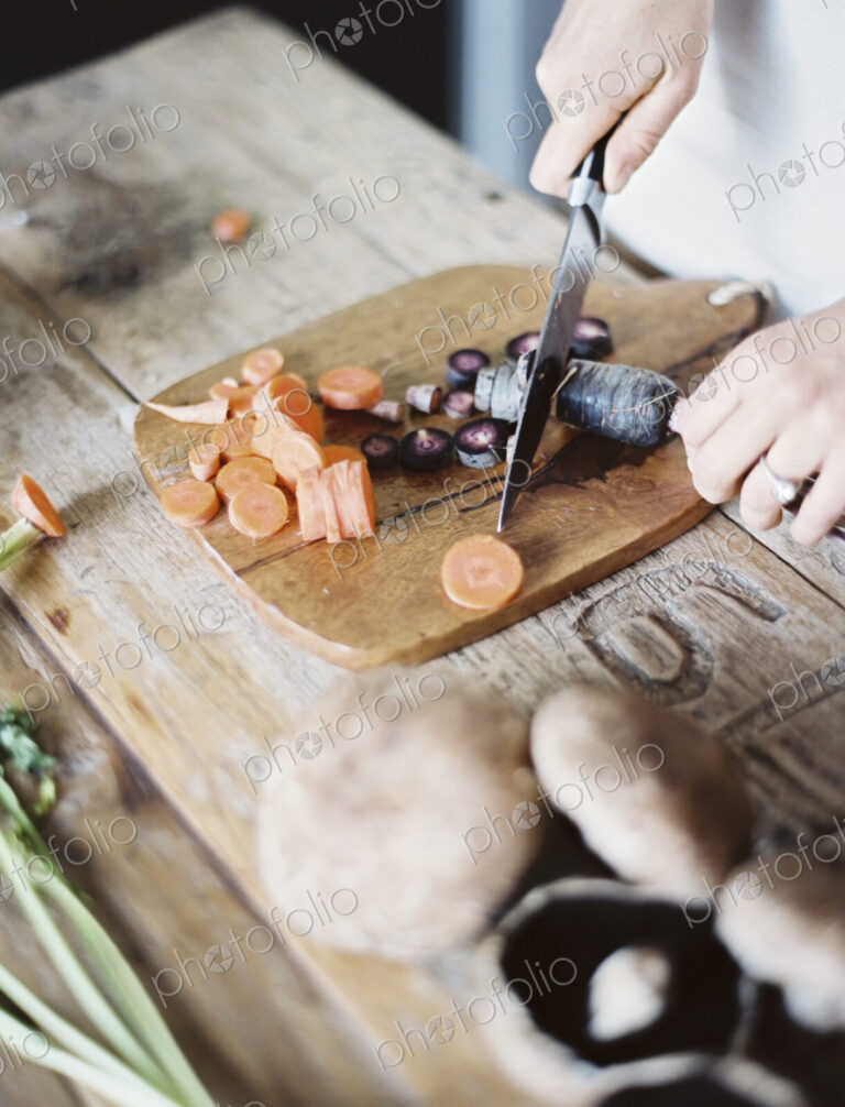 A domestic kitchen tabletop. A person chopping fresh vegetables on a chopping board…
