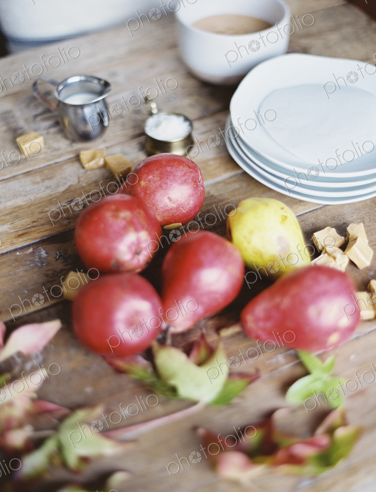 A domestic kitchen tabletop. A small group of fresh organic pears and a stack of white…