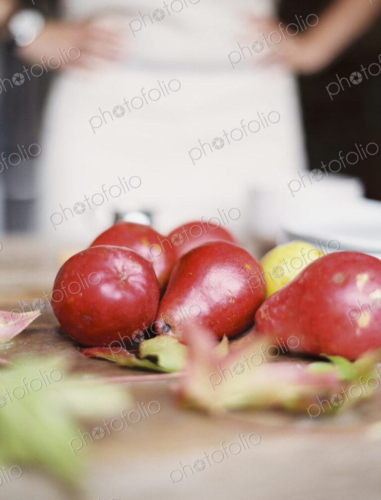 A domestic kitchen tabletop. A small group of fresh organic pears and a stack of white…