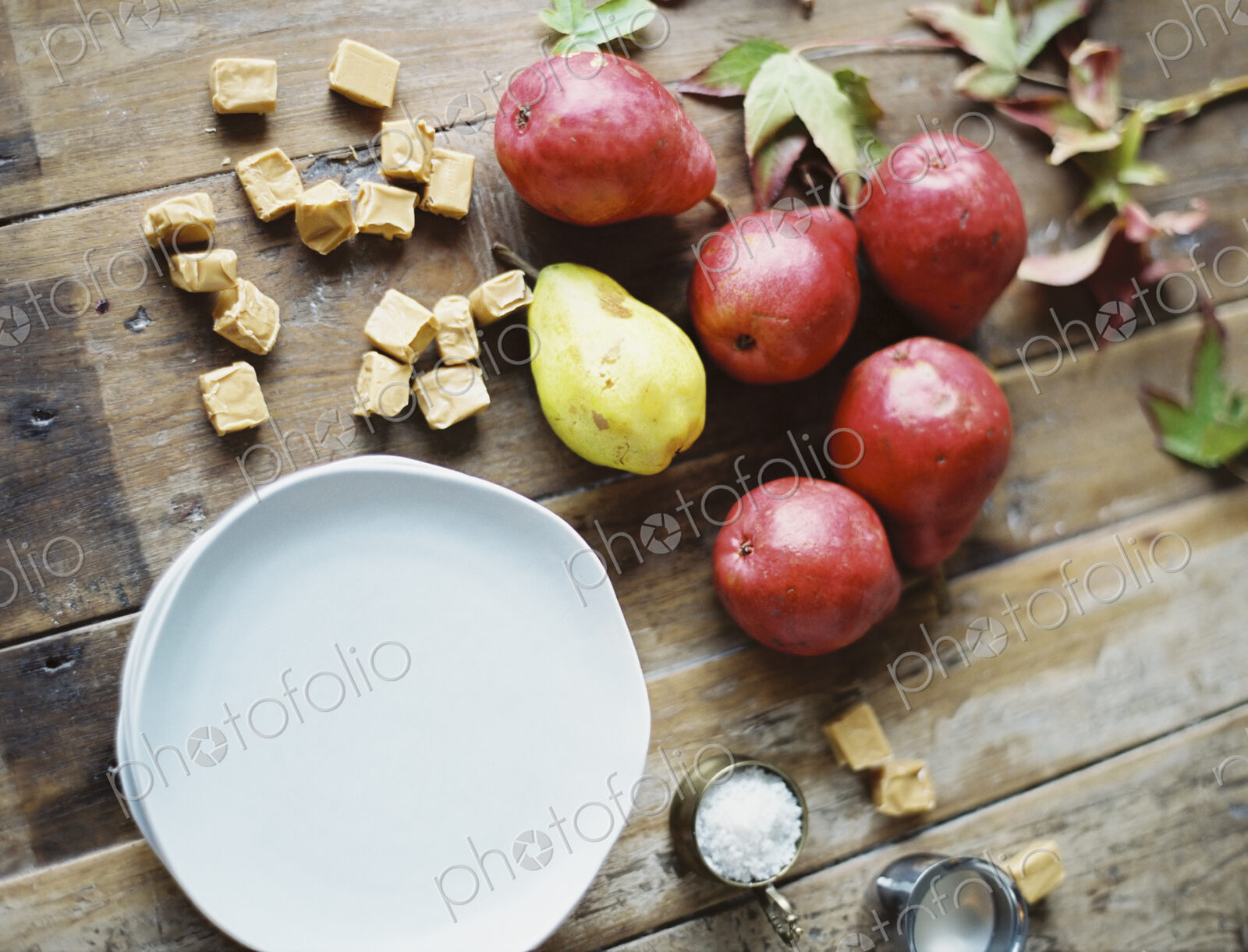 A domestic kitchen tabletop. A small group of fresh organic pears and a stack of white…