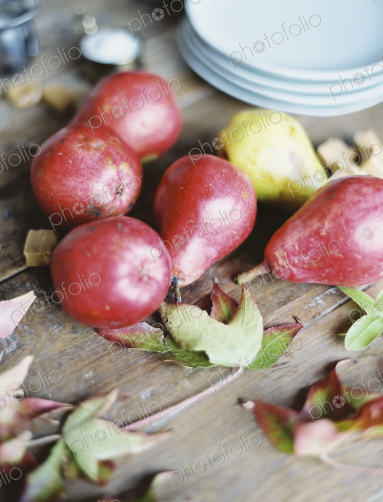 A domestic kitchen tabletop. A small group of fresh organic pears and a stack of white…