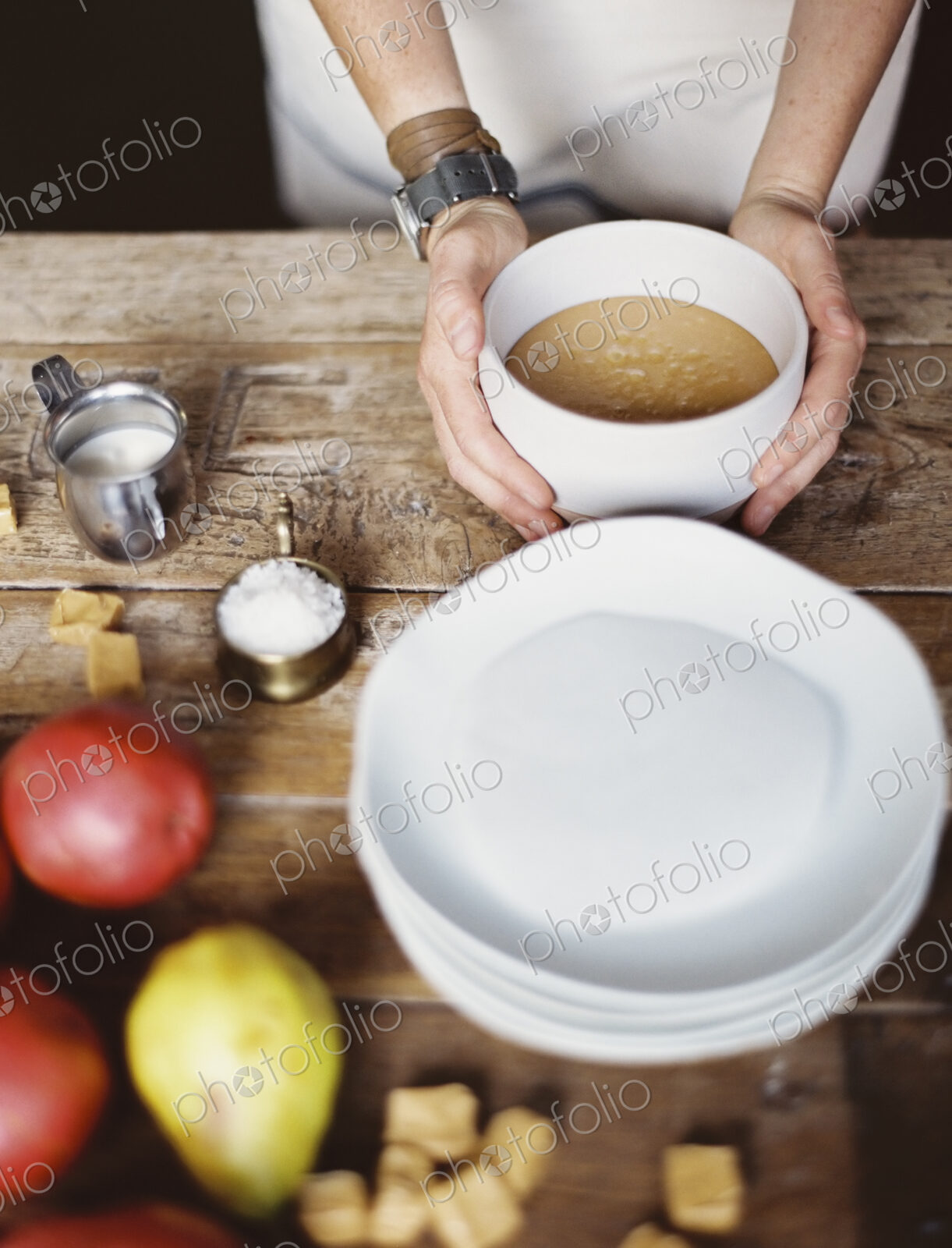 A domestic kitchen tabletop. A stack of white plates and fresh pears and a stack of…