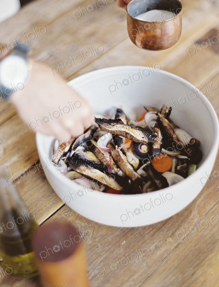 A domestic kitchen. A bowl of fresh chopped vegetables, in a white bowl. A person's…