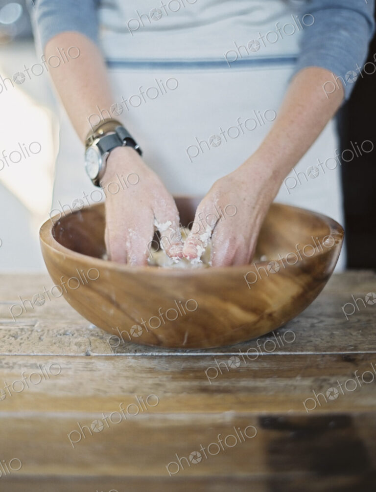 A domestic kitchen. A cook preparing pastry, mixing it by hand on a tabletop.