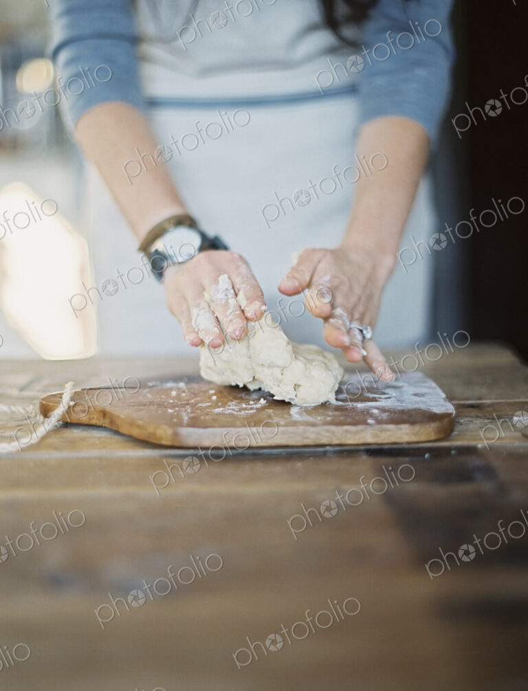 A domestic kitchen. A cook preparing pastry, mixing it by hand on a tabletop.