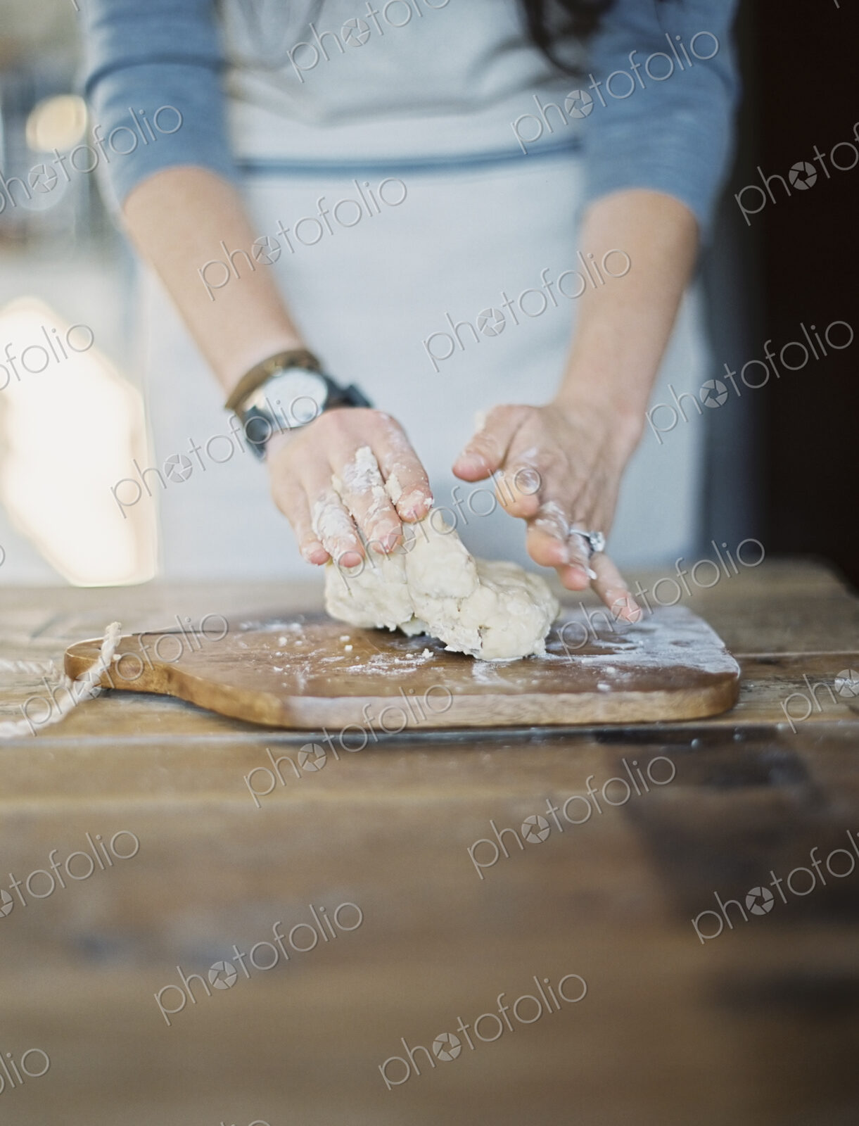 A domestic kitchen. A cook preparing pastry, mixing it by hand on a tabletop.