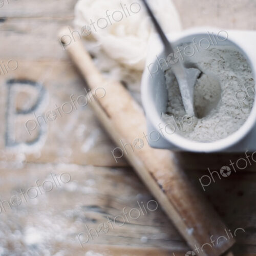 A domestic kitchen. A small group of objects. A rolling pin and jar of flour on a worn…