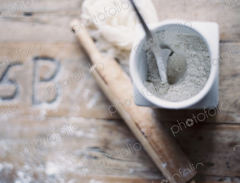 A domestic kitchen. A small group of objects. A rolling pin and jar of flour on a worn…