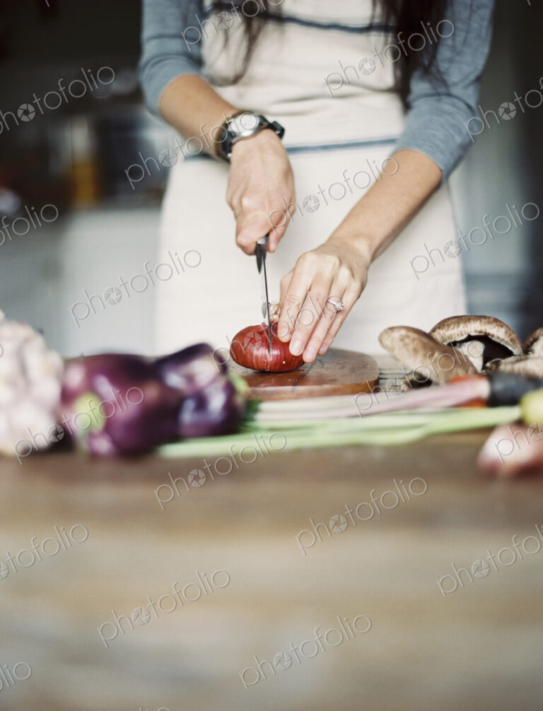 A domestic kitchen. A table top. Young woman chopping fresh vegetables with a knife.