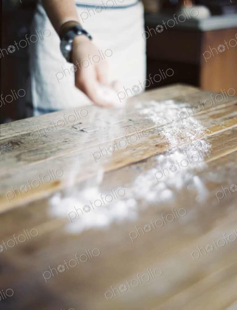 A domestic kitchen. A woman cooking. Spreading flour across a tabletop.