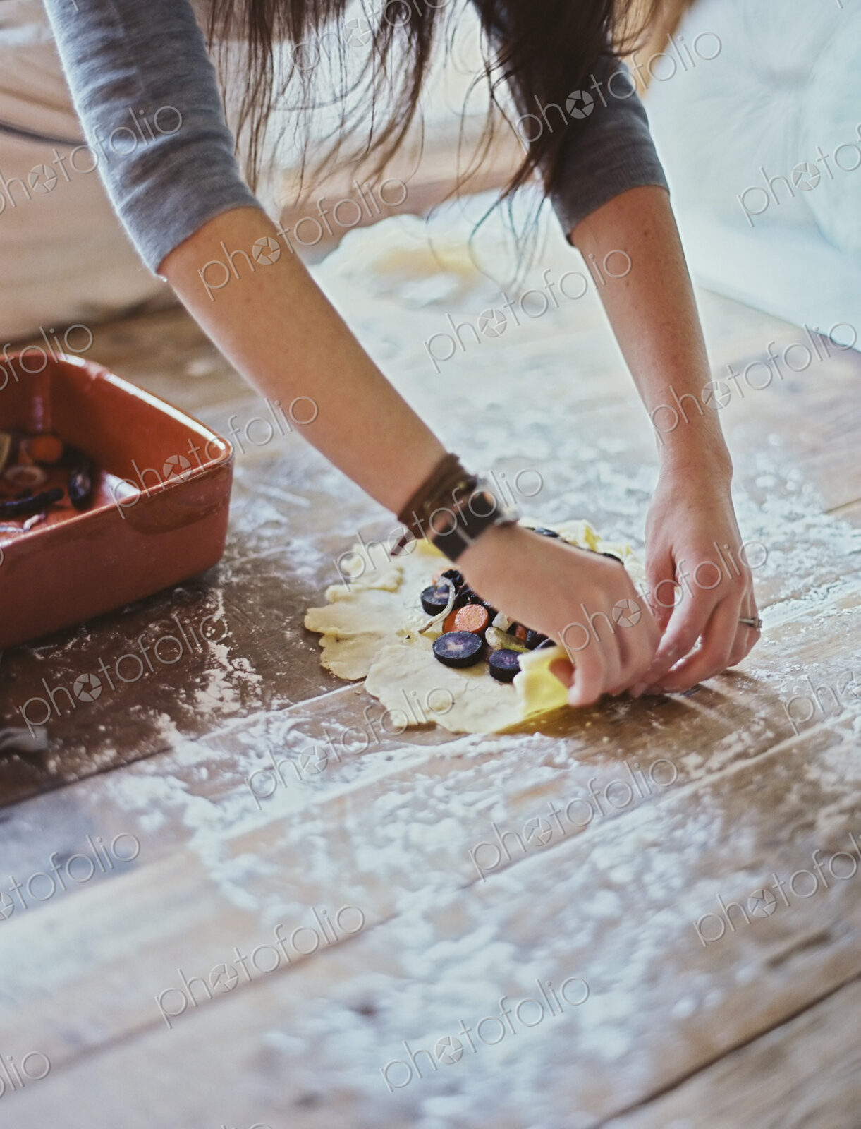 A domestic kitchen. A woman creating an open pastry tart with vegetables.