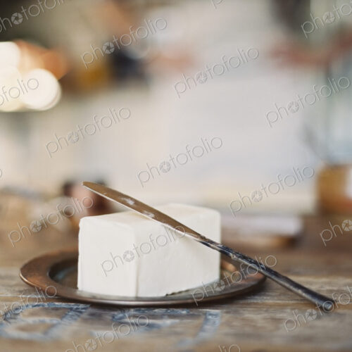 A domestic kitchen. A woman in the background. A slab of fresh organic butter, on a… A domestic kitchen. A woman in the background. A slab of fresh organic butter, on a…