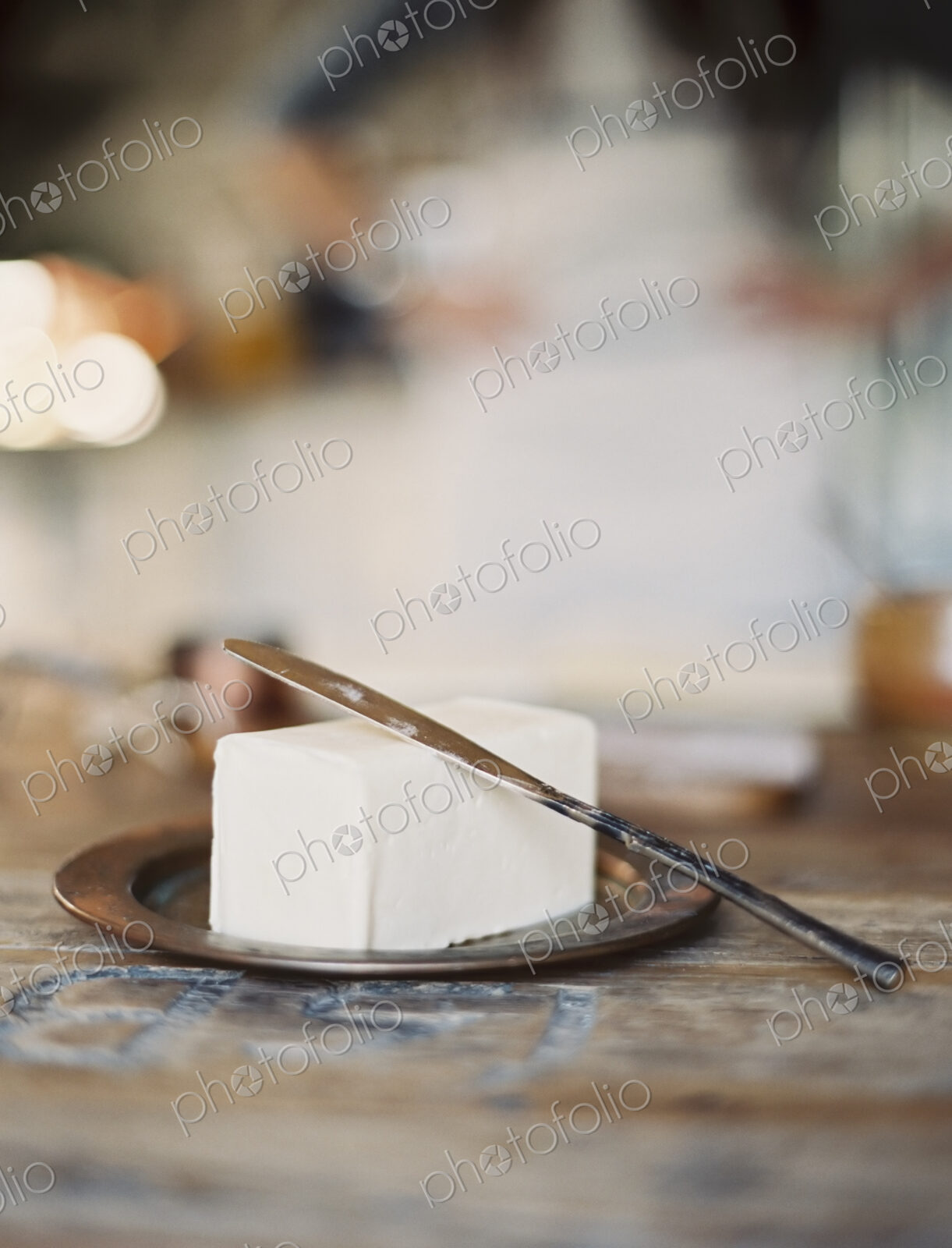 A domestic kitchen. A woman in the background. A slab of fresh organic butter, on a…