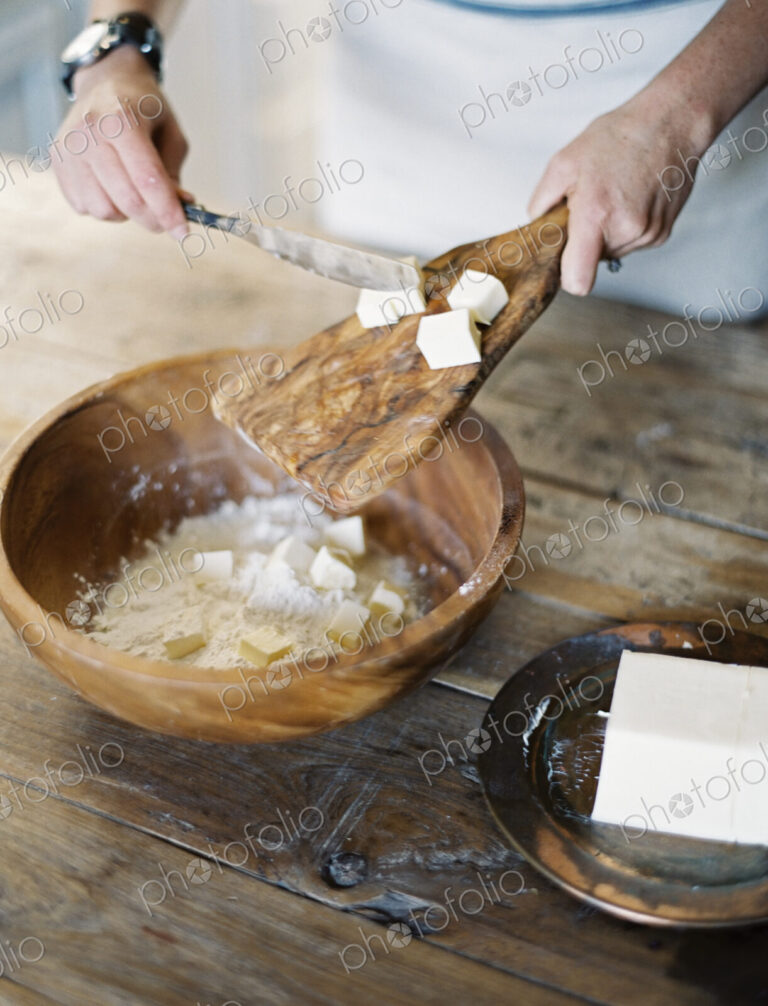 A domestic kitchen. A woman preparing a meal, mixing flour and fat to create pastry.