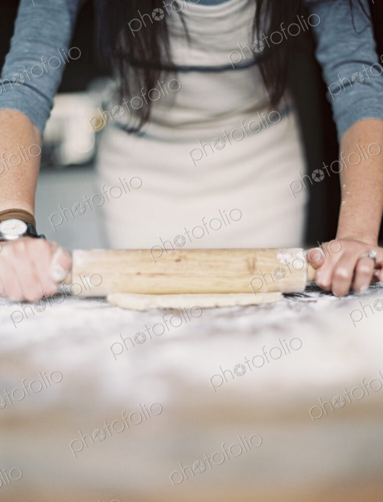 A domestic kitchen. A woman preparing a meal. Rolling out pastry on a table top.
