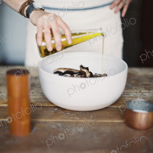 A domestic kitchen. A woman wearing an apron, dressing a fresh salad of vegetables in… A domestic kitchen. A woman wearing an apron, dressing a fresh salad of vegetables in…